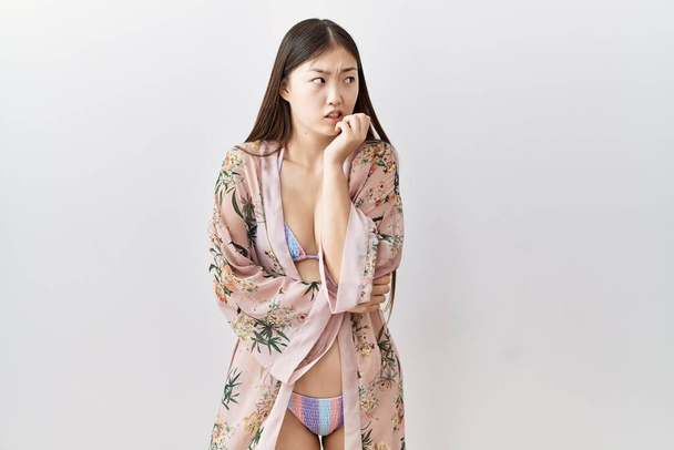 Genç Asyalı kadın bikini giyiyor ve çiçek kimonosu giyiyor. Gergin ve gergin görünüyor. Elleri ağızdan tırnak yiyor. anksiyete.  - Fotoğraf, Görsel