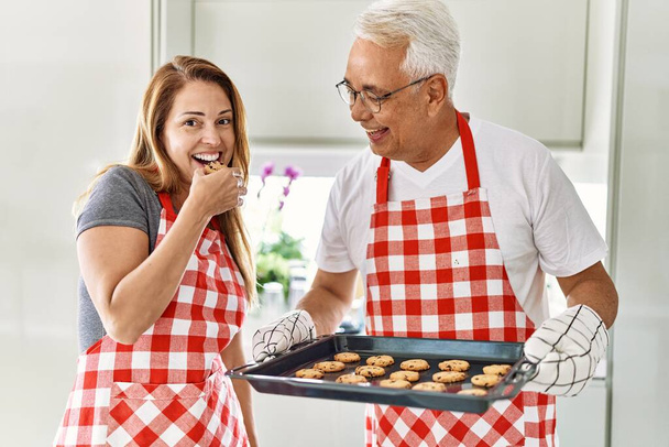 Latynoska para w średnim wieku uśmiechnięta szczęśliwa piekąc ciasteczka w kuchni. - Zdjęcie, obraz