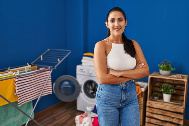Young hispanic woman at laundry room happy face smiling with crossed arms looking at the camera. positive person.  - Fotó, kép