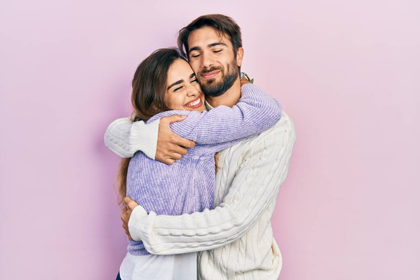 Jong Latijns-Amerikaans echtpaar dat casual kleding draagt en zich vrolijk en positief omhelst, vol zelfvertrouwen glimlacht. zelfliefde en zelfzorg  - Foto, afbeelding