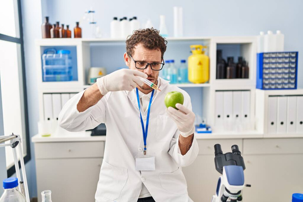Mladý hispánec muž vědec vstřikování tekutiny na jablko v laboratoři - Fotografie, Obrázek