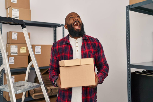 Αφροαμερικάνος που εργάζεται σε μικρές επιχειρήσεις ecommerce θυμωμένος και τρελός ουρλιάζοντας απογοητευμένοι και έξαλλος, φωνάζοντας με θυμό κοιτάζοντας ψηλά.  - Φωτογραφία, εικόνα