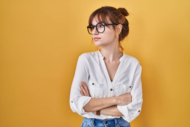 Young beautiful woman wearing casual shirt over yellow background looking to the side with arms crossed convinced and confident  - Photo, Image