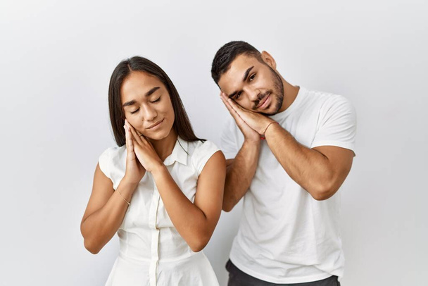 Young interracial couple standing together in love over isolated background sleeping tired dreaming and posing with hands together while smiling with closed eyes.  - Photo, Image