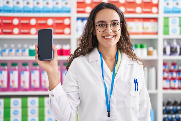 Mladý krásný hispánský žena lékárník ukazující smartphone app v lékárně - Fotografie, Obrázek