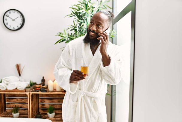 Young african american man talking on the smartphone drinking champagne at beauty center - Photo, Image