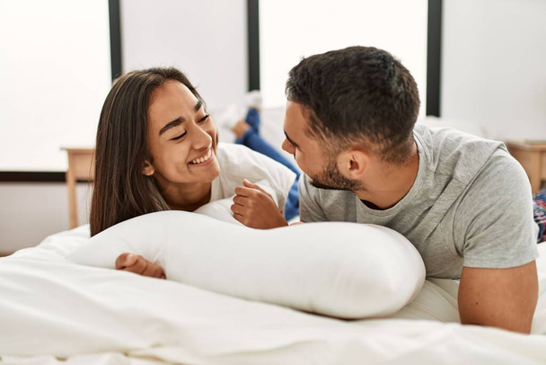 Jeune couple latino souriant heureux étreinte sur le lit à la maison. - Photo, image