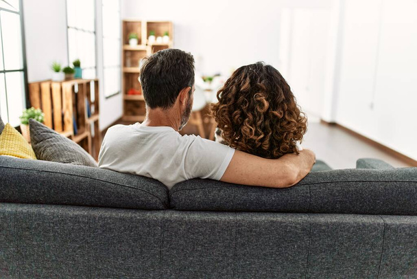 Middle age hispanic couple on back view hugging and sitting on the sofa at home. - Fotó, kép