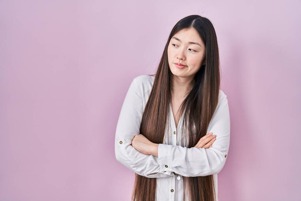 Chinese jonge vrouw staan over roze achtergrond kijken naar de zijkant met armen gekruist overtuigd en vol vertrouwen  - Foto, afbeelding