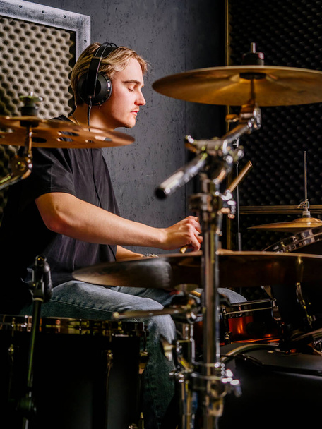 Young man wearing headphones and playing drums in a recording studio. - Fotografie, Obrázek