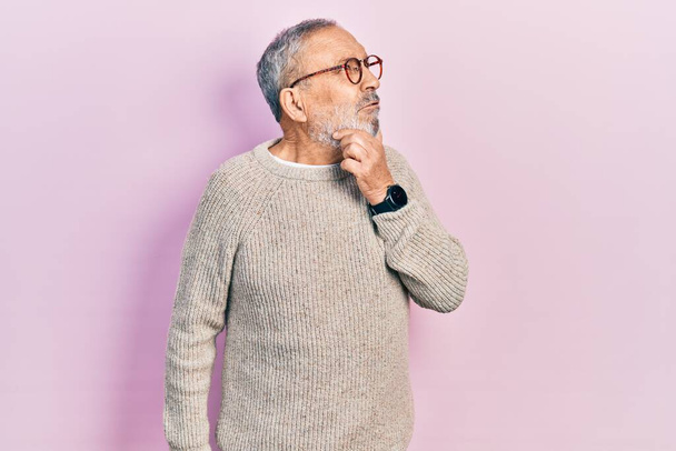 Όμορφος ηλικιωμένος άντρας με γενειάδα που φοράει περιστασιακό πουλόβερ και γυαλιά που σκέφτεται ανησυχώντας για μια ερώτηση, ανήσυχος και νευρικός με το χέρι στο πηγούνι  - Φωτογραφία, εικόνα