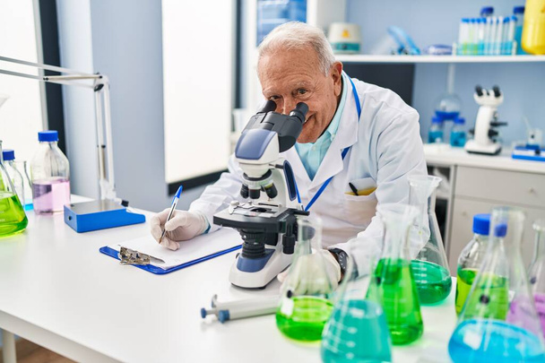 Homme âgé portant l'uniforme de scientifique utilisant le microscope au laboratoire - Photo, image
