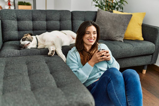 Νεαρή γυναίκα πόσιμο έγχυση σύντροφο κάθεται με το σκυλί στο σπίτι - Φωτογραφία, εικόνα