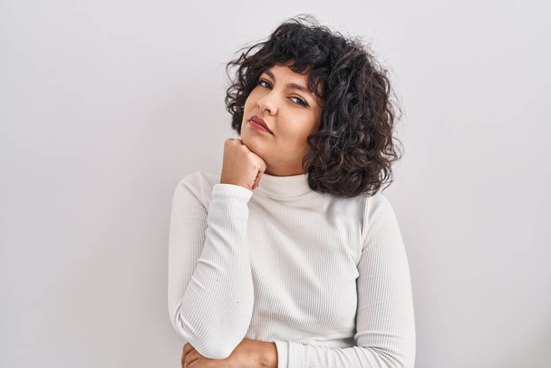 Hispanic woman with curly hair standing over isolated background with hand on chin thinking about question, pensive expression. smiling with thoughtful face. doubt concept.  - Photo, Image