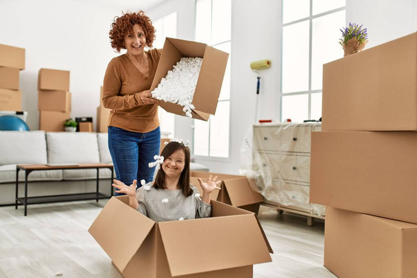 Mature mother and down syndrome daughter moving to a new home, having fun with cardboard foam - Photo, Image