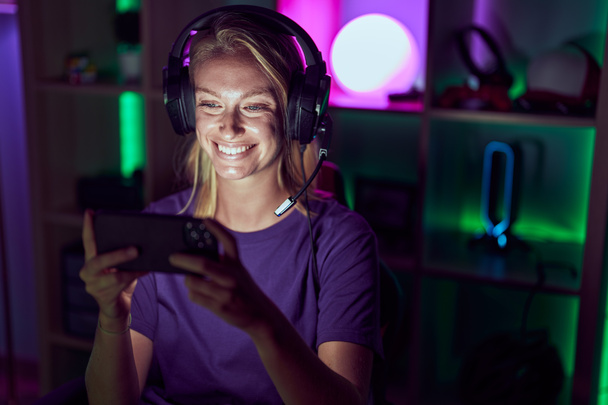 Νεαρή ξανθιά γυναίκα streamer χαμογελά αυτοπεποίθηση παίζοντας βιντεοπαιχνίδι στην αίθουσα τυχερών παιχνιδιών - Φωτογραφία, εικόνα