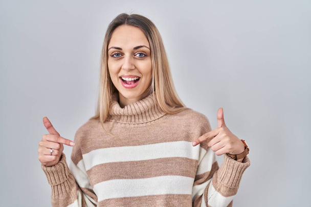 Mladá blondýna žena na sobě rolák svetr přes izolované pozadí vypadá sebevědomě s úsměvem na tváři, ukazuje se s prsty hrdý a šťastný.  - Fotografie, Obrázek