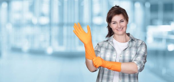 Η έννοια της έναρξης των υπηρεσιών καθαρισμού. Καθαρίστρια που φοράει λαστιχένιο γάντι σε θολή φόντο. - Φωτογραφία, εικόνα