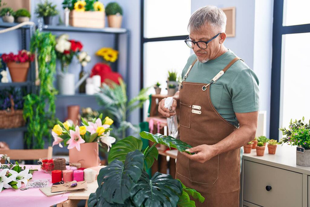 Middle age grey-haired man florist using difusser working at flower shop - Foto, Bild