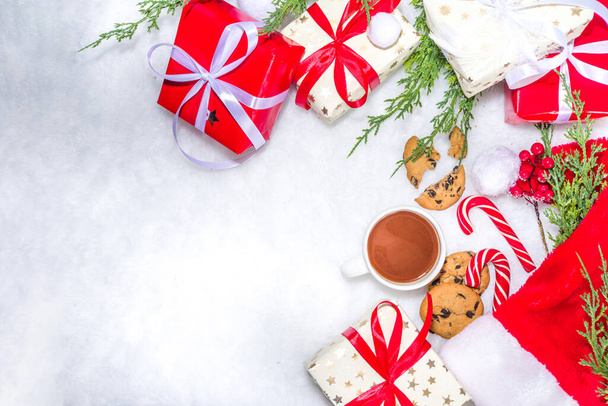 Kreatív elrendezés keret sok ajándék dobozok, karácsonyfa ágak, fenyőtoboz, forró csokoládé bögre, Xmas édes, tabletta pc fehér bolyhos szőrme háttér. Karácsonyi és újévi felkészülés háttér - Fotó, kép