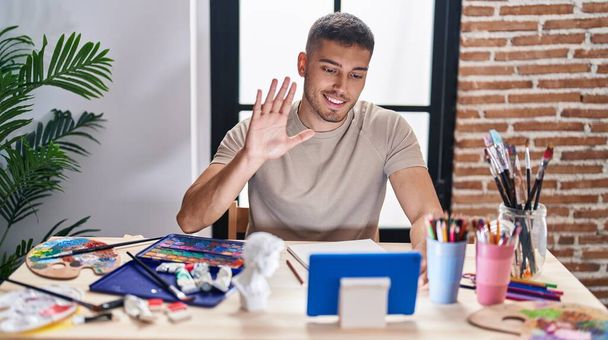 Young hispanic painter man doing online call with tablet looking positive and happy standing and smiling with a confident smile showing teeth  - Photo, Image