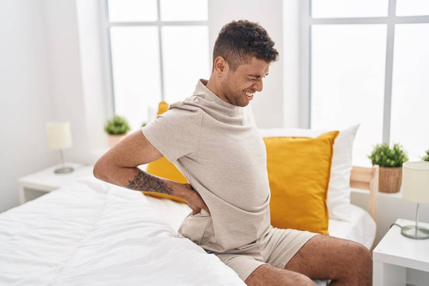 Afroamerikaner leidet unter Rückenschmerzen, wenn er im Schlafzimmer im Bett sitzt - Foto, Bild