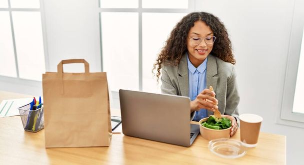 Young latin woman smiling confident eating salad at office - Photo, Image