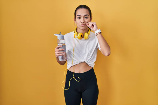 Junge südasiatische Frau in Sportkleidung trinkt Wasser Mund und Lippen als Reißverschluss mit den Fingern geschlossen. Geheimniskrämerei und Schweigen, Tabuthema  - Foto, Bild
