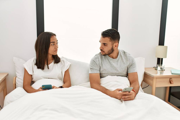 Junges lateinisches Paar mit Smartphone zu Hause im Bett liegend. - Foto, Bild