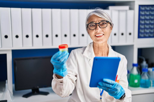 Седовласая женщина-ученый средних лет с помощью пробирки для тачпада в лаборатории - Фото, изображение