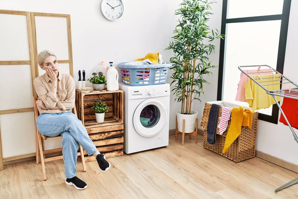 Young caucasian woman boring waiting for washing machine at laundry room - Foto, Bild