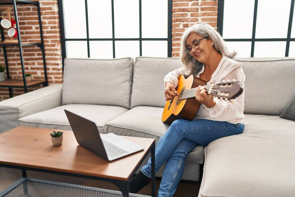 Keski-ikäinen nainen, jolla on online kitara luokan kotona - Valokuva, kuva