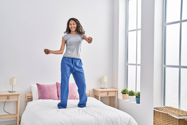 Молодая африканская американка улыбается уверенно танцуя на кровати в спальне - Фото, изображение