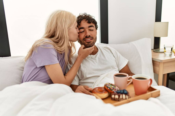 Joven hermosa pareja sonriendo feliz desayunando en la cama en casa. - Foto, Imagen