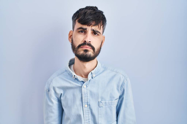 Young hispanic man with beard standing over blue background depressed and worry for distress, crying angry and afraid. sad expression.  - Foto, afbeelding