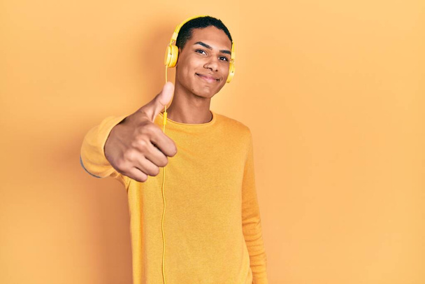 Fiatal afro-amerikai srác zenét hallgat fejhallgatóval, és boldog hüvelykujjával kézmozdulatot tesz. jóváhagyása kifejezés nézi a kamera mutatja siker.  - Fotó, kép