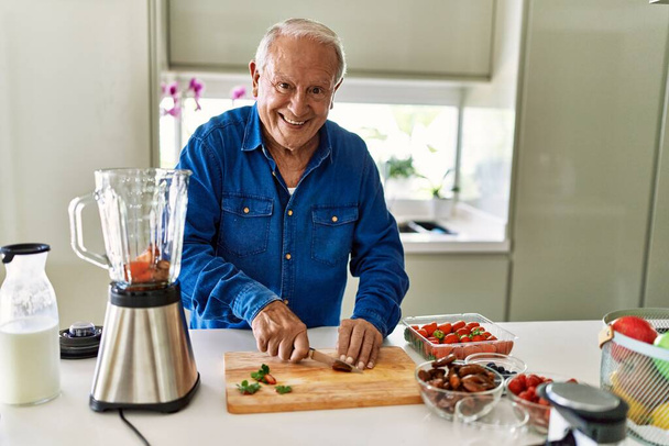 Senior man smiling confident cutting datil at kitchen - Fotó, kép