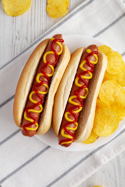 Homemade Hot Dog with Ketchup and Yellow Mustard with Chips on a Plate, top view. Flat lay, overhead, from above. - Foto, Bild