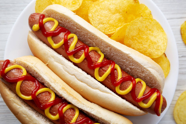 Homemade Hot Dog with Ketchup and Yellow Mustard with Chips on a Plate, top view. Flat lay, overhead, from above. Close-up. - Photo, Image