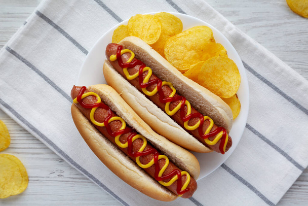 Homemade Hot Dog with Ketchup and Yellow Mustard with Chips on a Plate, top view. Flat lay, overhead, from above. - Foto, immagini