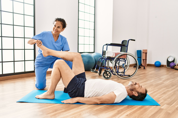 Middelbare leeftijd man en vrouw glimlachend zelfverzekerd na revalidatie sessie stretching in fysiotherapie kliniek - Foto, afbeelding
