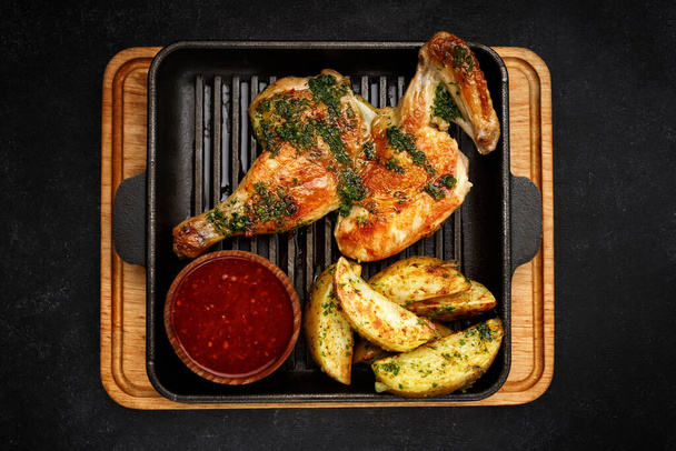 Half a grilled chicken with fried potatoes and barbecue sauce in a pan - Foto, Bild