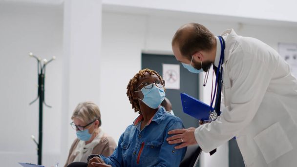 Hekim, Afro-Amerikan kadınını Coronavirus salgını sırasında muayeneye götürüyor. Sıhhiye tavsiye veriyor ve klinikte kovid 19 korumasında hastaya yardım ediyor. El kamerasıyla.. - Fotoğraf, Görsel