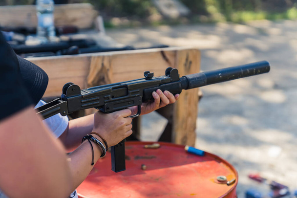 Unrecognizable young person holding uzi gun training on shooting range under supervision. Horizontal outdoor shot. High quality photo - Fotó, kép
