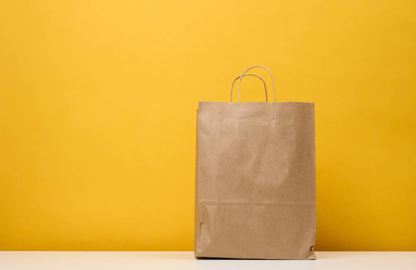 A brown paper bag stands on a white table, yellow background. Product packaging - 写真・画像