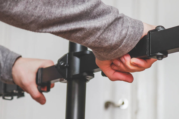 The hands of a young Caucasian guy sets up a bracket for a monitor in his room with a blurred background of doors and selective focus, bottom view. Home renovation concept. - Foto, Bild