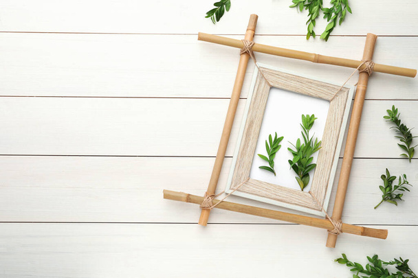 Flat lay composition with bamboo frame and green leaves on white wooden table. Space for text - 写真・画像
