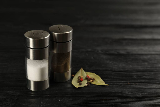 Salt and pepper shakers with bay leaves on black wooden table, closeup. Space for text - Photo, image