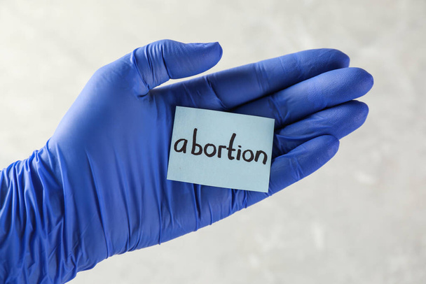 Doctor holding paper card with word ABORTION on light background, closeup - Фото, зображення