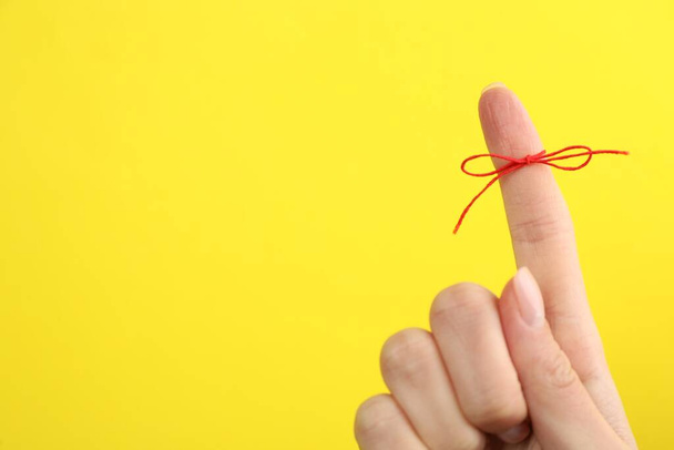 Woman showing index finger with tied red bow as reminder on yellow background, closeup. Space for text - 写真・画像
